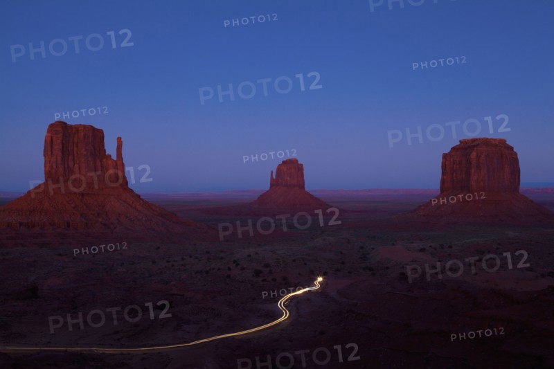 Long exposure of car driving past butte rock formations in desert landscape