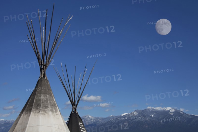 Teepees under full moon in blue sky