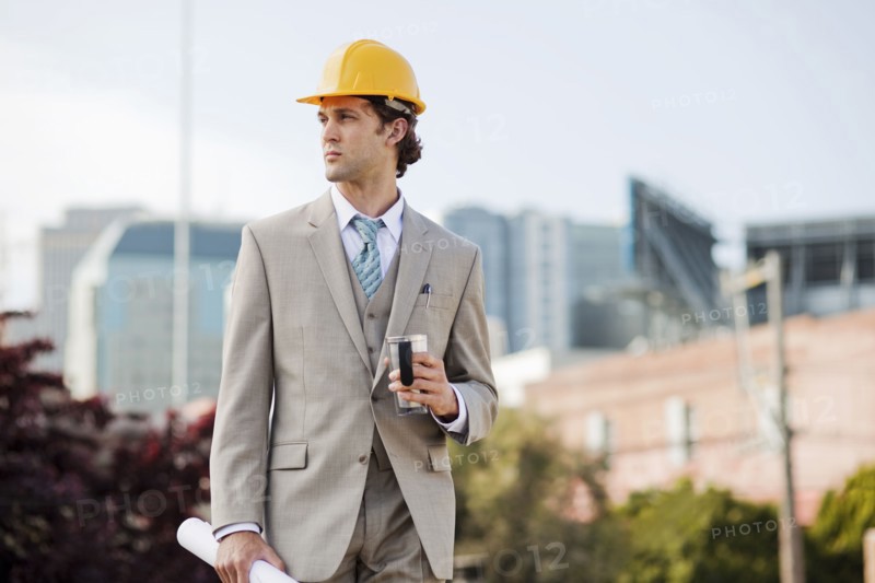 Hispanic businessman drinking coffee and carrying blueprint outdoors