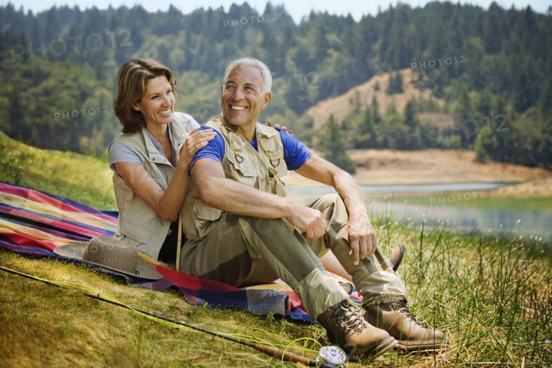Couple sitting on blanket near lake with fishing rod