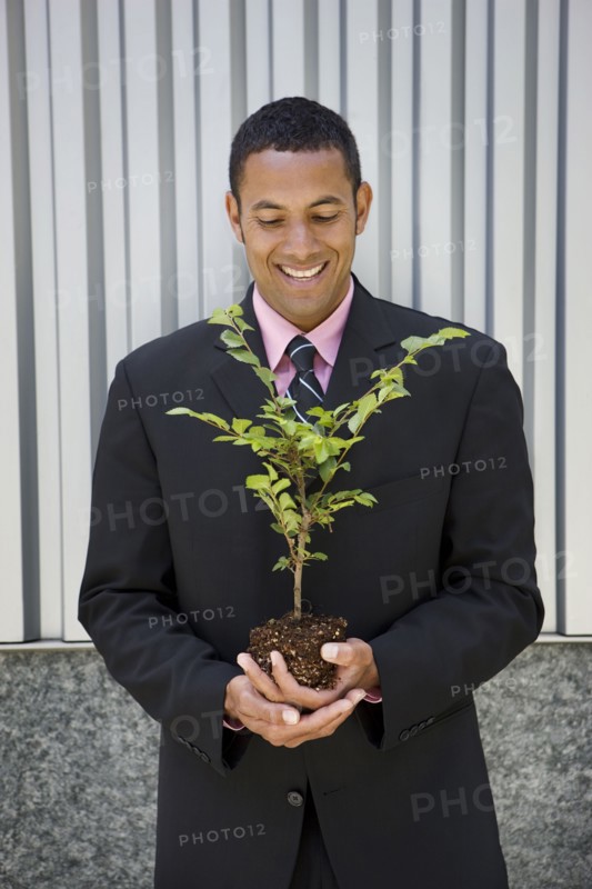 Smiling mixed race businessman holding seedling