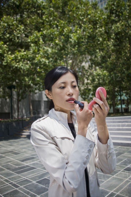 Asian woman applying lipstick outdoors