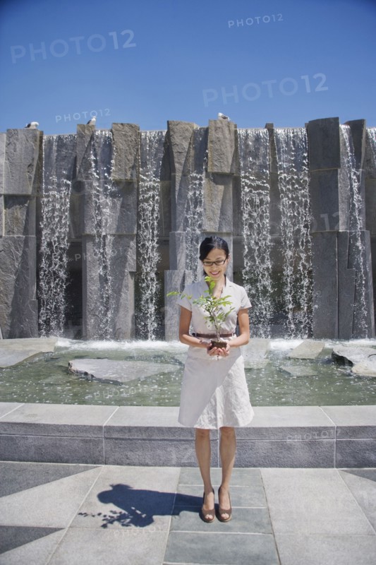 Asian woman holding seedling near fountain