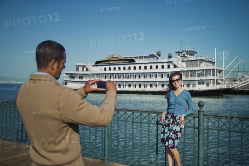 Man photographing woman at waterfront