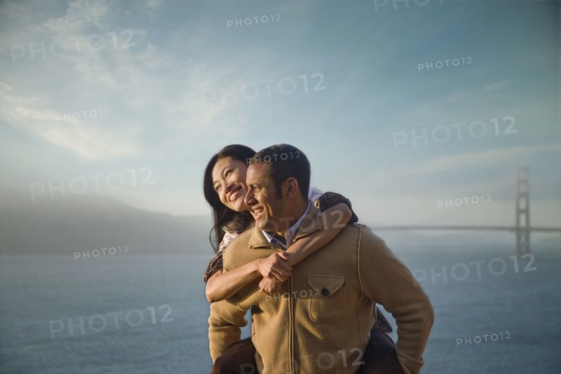 Man carrying woman piggyback near bay