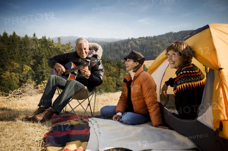 Women at camping tent listening to man playing guitar