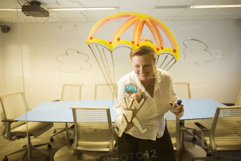 Caucasian businesswoman drawing a golden parachute on conference room wall
