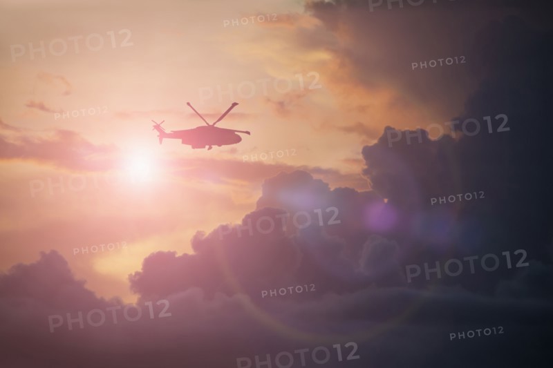 Silhouette of helicopter flying in cloudy sky