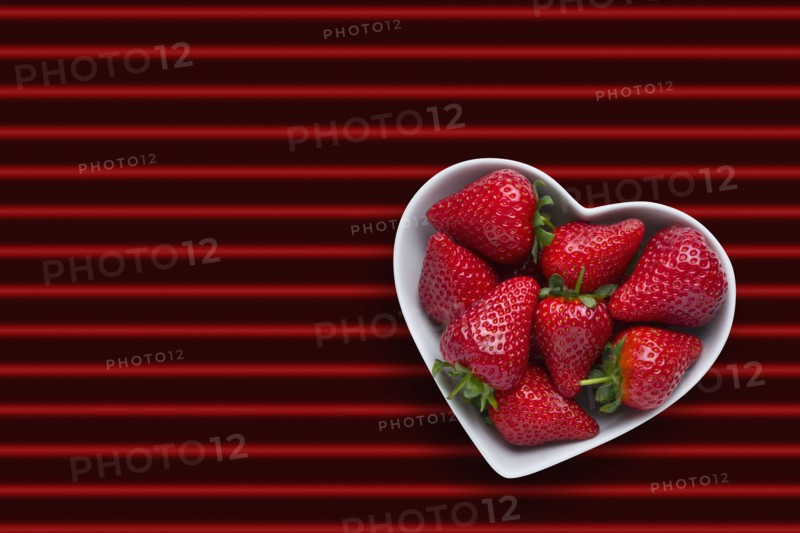Strawberries in heart-shape bowl on red striped background