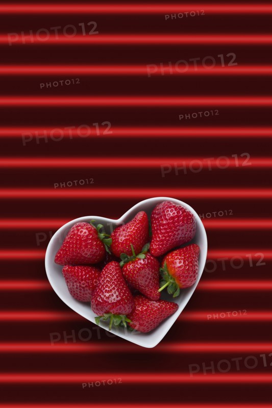 Strawberries in heart-shape bowl on red striped background