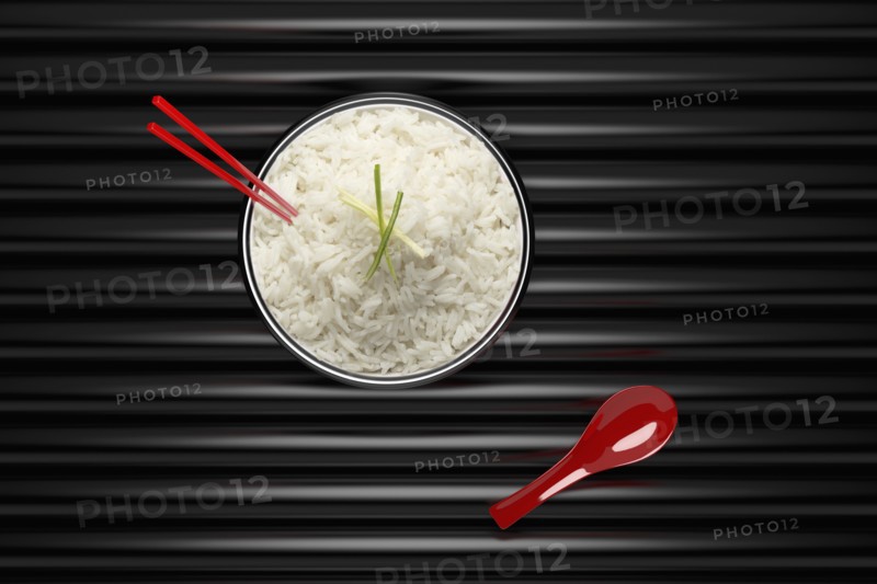 Chopsticks in bowl of white rice with red spoon