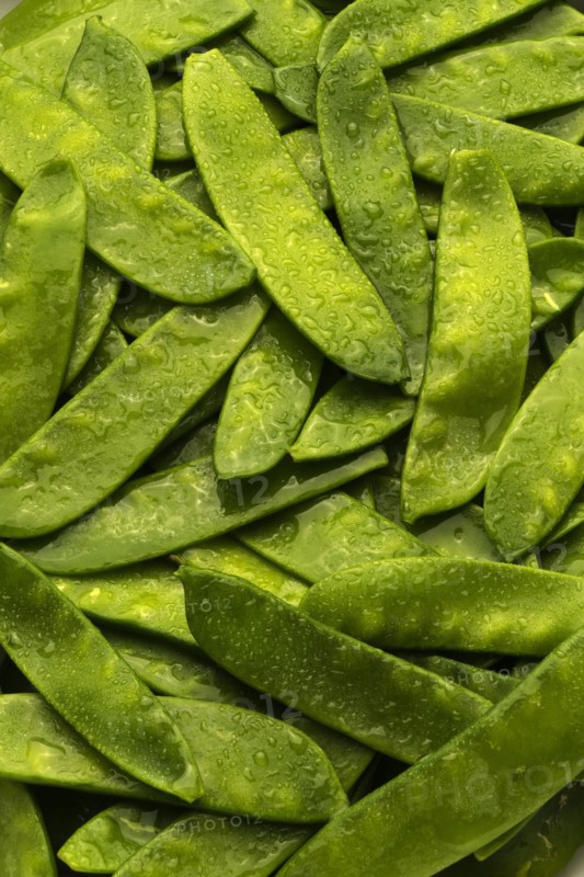 Pile of wet green peas in pods