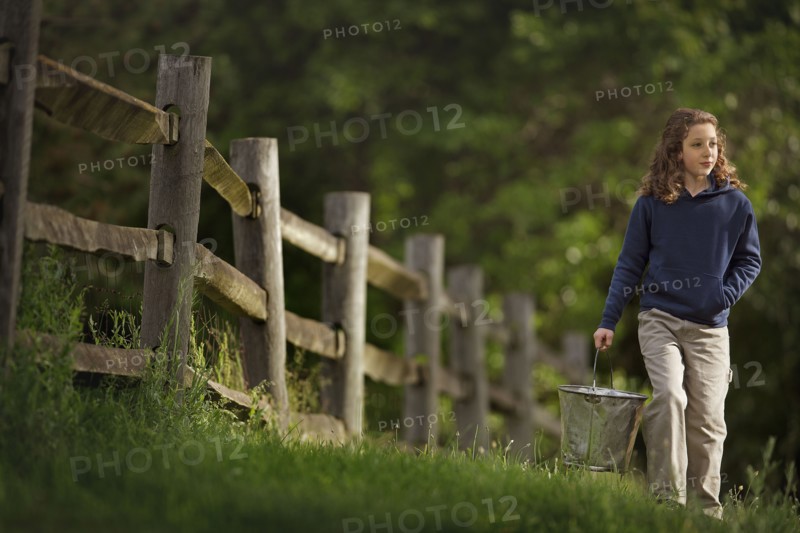 Caucasian girl carrying bucket near wooden fence