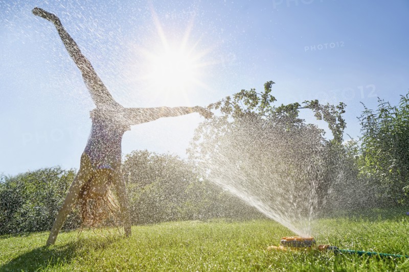Caucasian girl performing cartwheel through backyard sprinkler