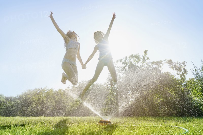 Caucasian girls jumping over backyard sprinkler