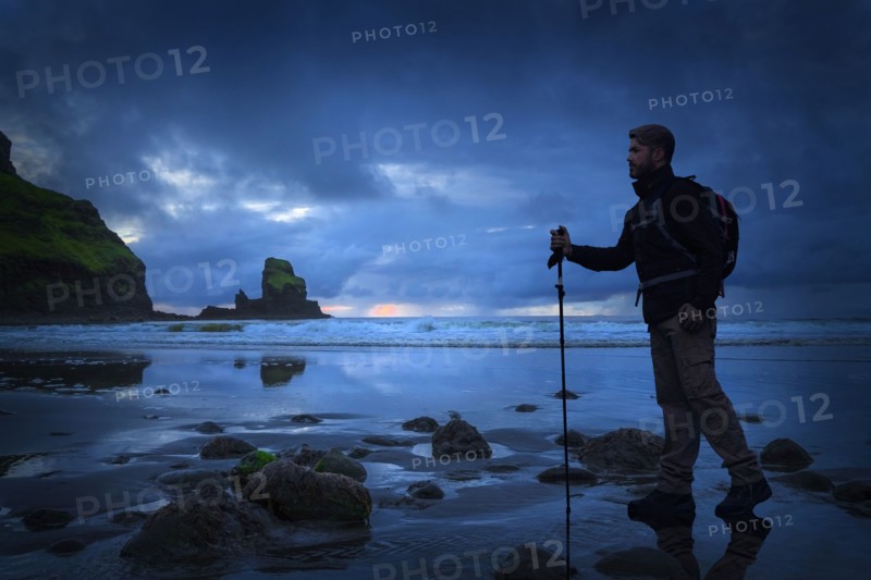 Caucasian hiker standing on beach at sunset