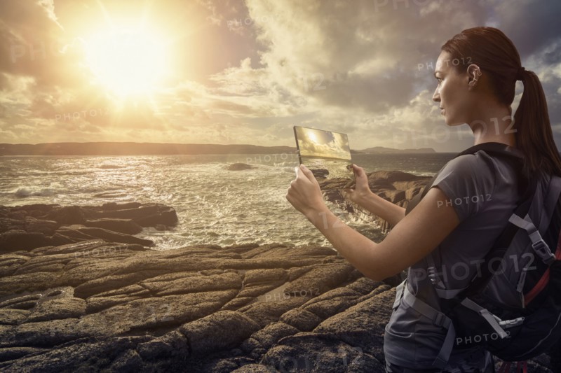 Caucasian woman photographing ocean sunset with digital tablet