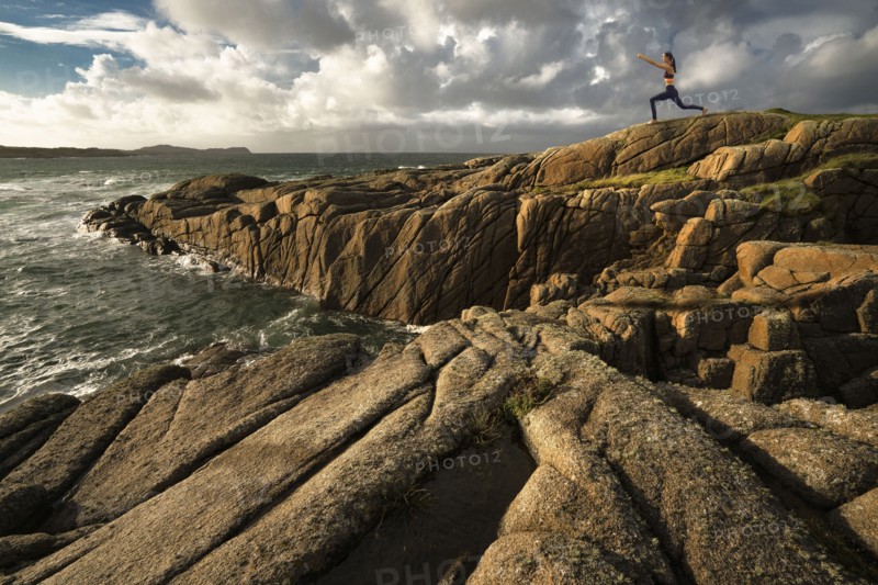 Distant Caucasian woman doing yoga on rocks near ocean