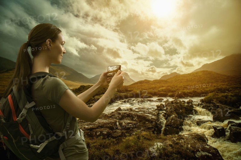 Caucasian woman photographing mountain river with cell phone