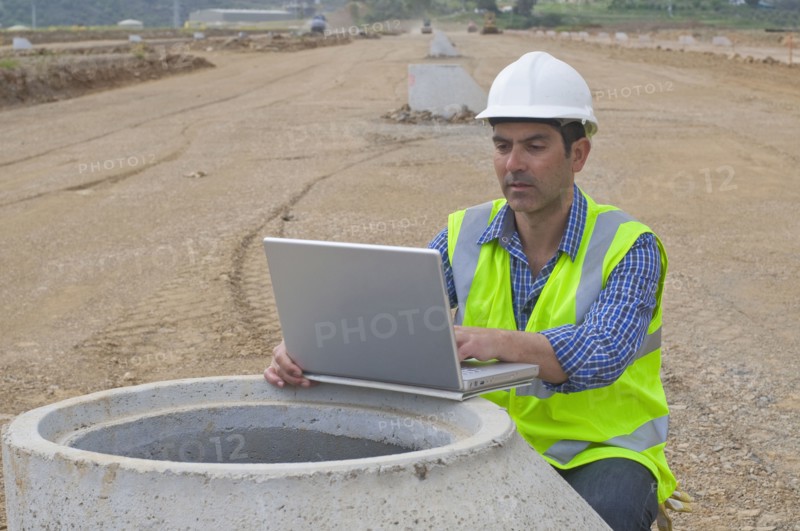 Hispanic construction worker using laptop in field