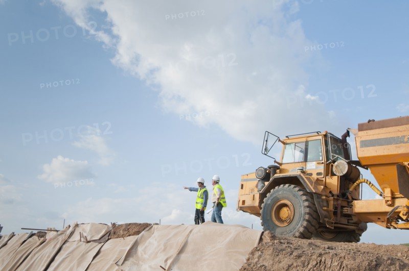 Hispanic construction workers in field with dump truck