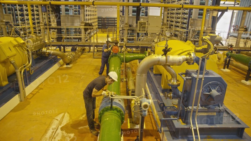 Hispanic workers examining pipes in factory