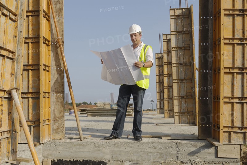 Male engineer wearing hard hat looking at plans on building site