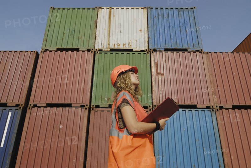 Female worker with clipboard in cargo container terminal low angle