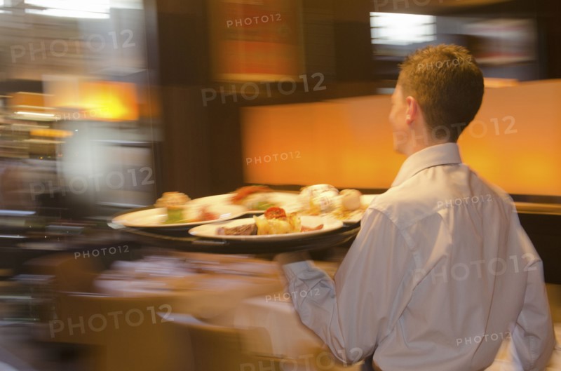 Waiter carrying tray with dishes through resturant