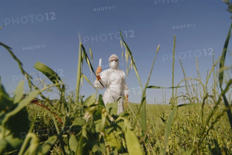 Woman in boiler suit standing in field holding test tube