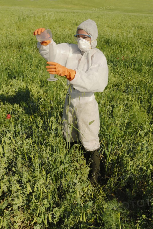 Woman in boiler suit standing in field pouring liquid into test tube