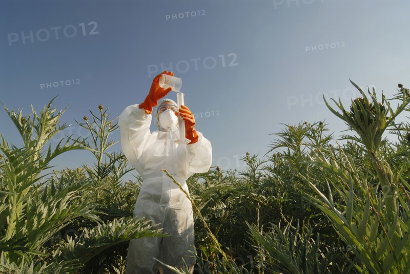 Woman in boiler suit standing in field pouring liquid into test tube