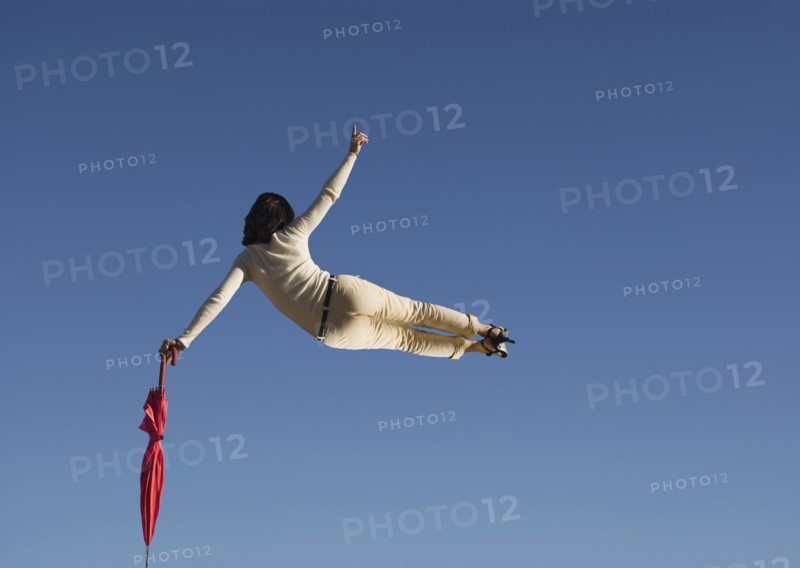 Woman in mid air clicking heels holding umbrella rear view