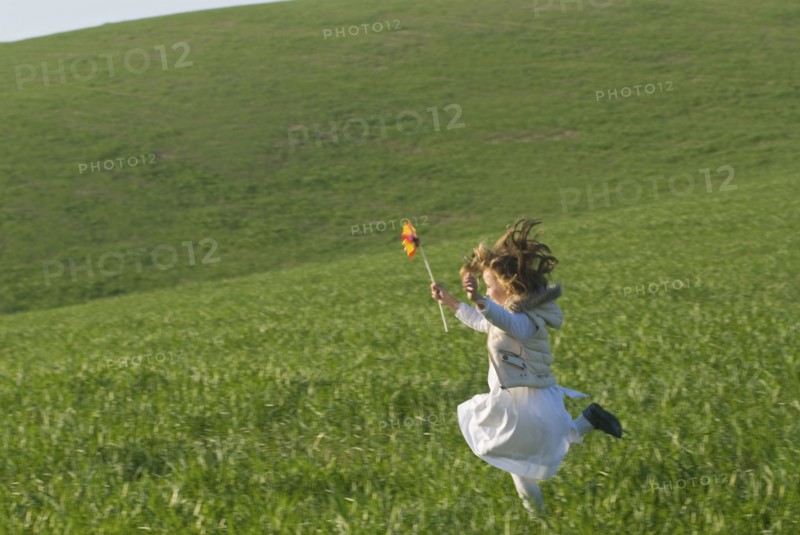 young girl with wind wheel running in green fields