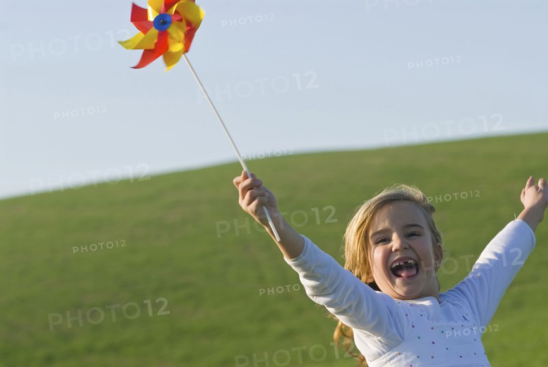 young girl with wind wheel running in green fields