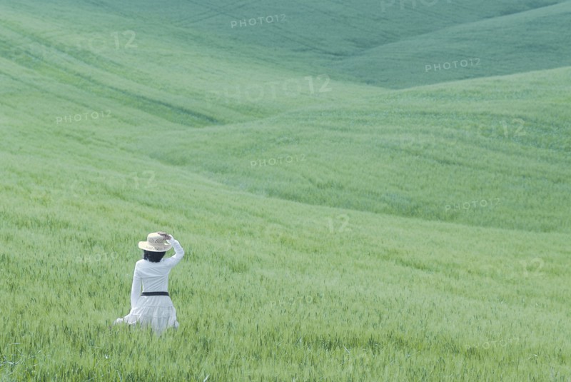 Woman in white dress walking through rolling hills of young wheat