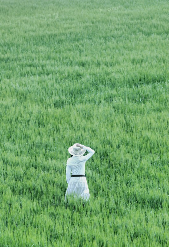 Woman wearing hat standing in field rear view