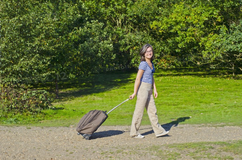 woman walking though park pulling roller case