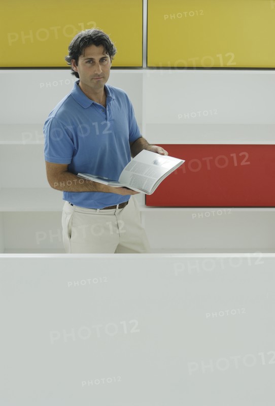 Male office worker holding book in front of coloured shelves portrait