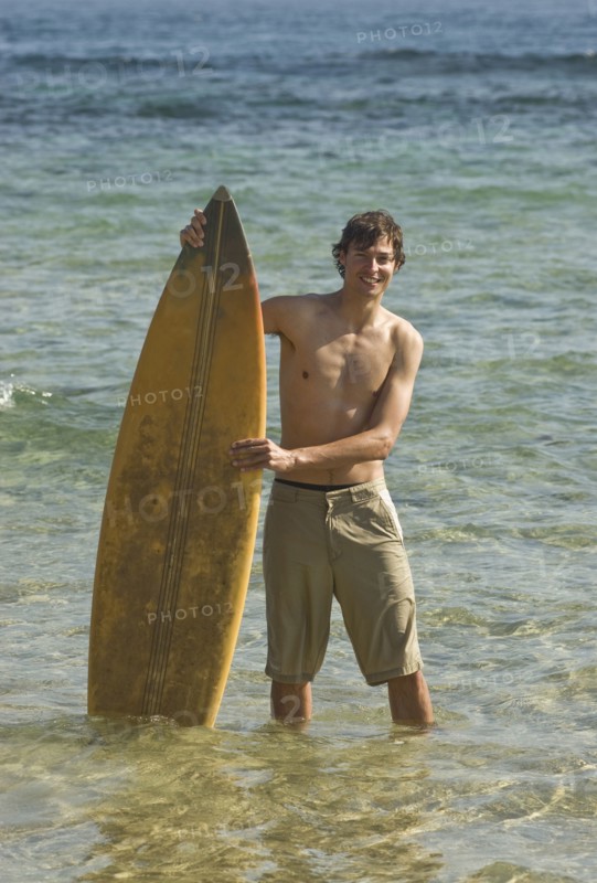 Young surfer standing in water holding surfboard portrait