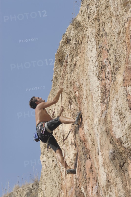 Male rock climber scaling rock face secured by ropes low angle view