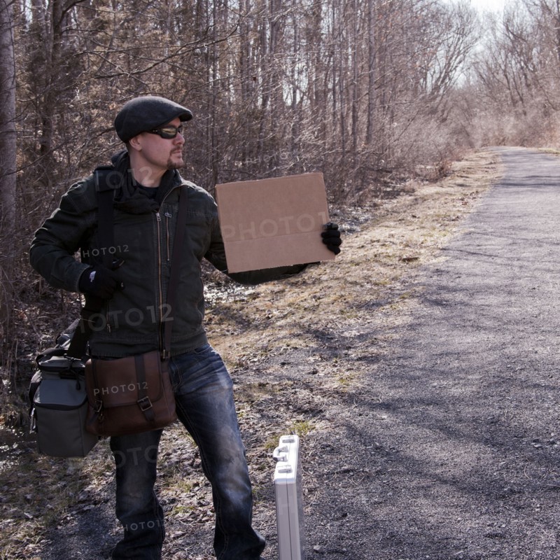 Man hitchhiking with blank sign on rural road