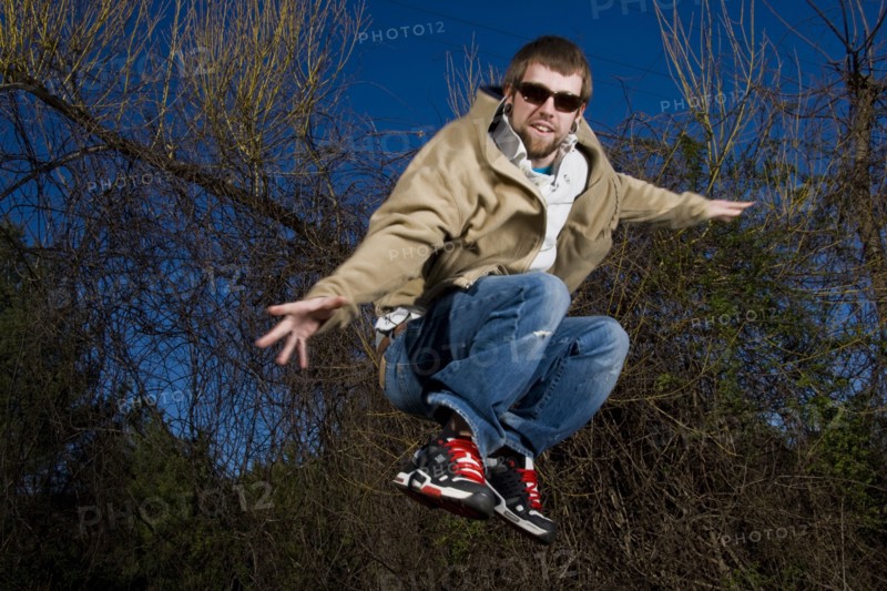 Man wearing sunglasses jumping for joy in forest