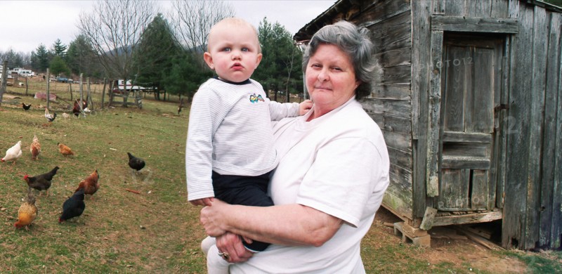 Grandmother carrying grandson near chicken coop on farm