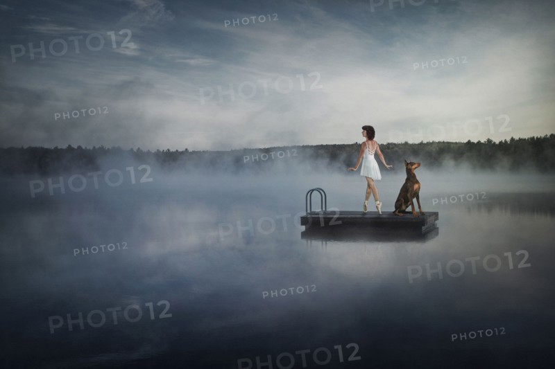 Caucasian ballet dancer on floating dock in foggy lake with dog