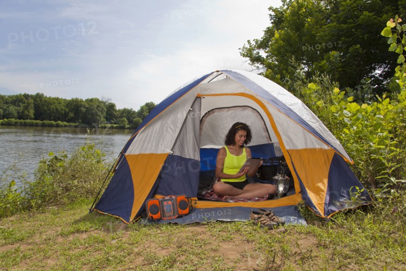 Hispanic woman using digital tablet in camping tent at lake