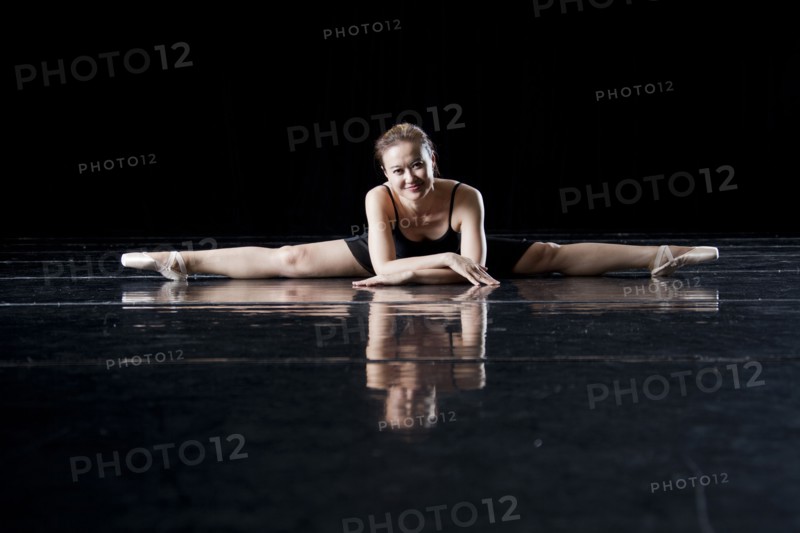 Asian ballerina laying on floor doing splits on dark stage