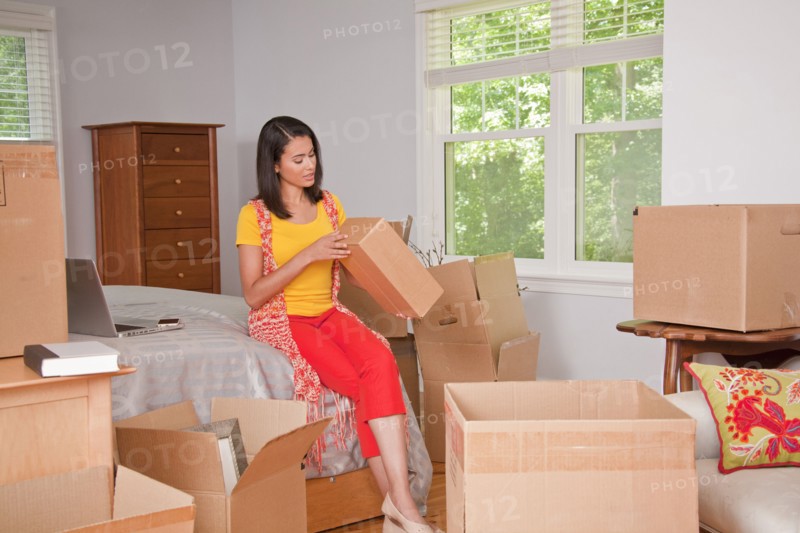 Hispanic woman examining cardboard box in bedroom