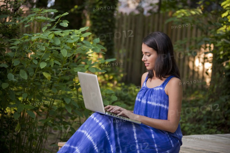 Smiling Hispanic woman using laptop on patio in backyard