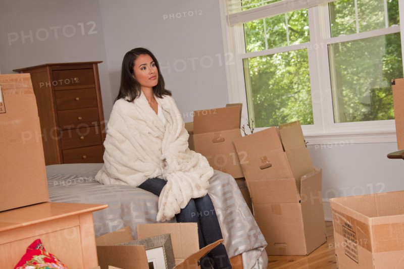 Pensive Hispanic woman sitting on bed near moving boxes